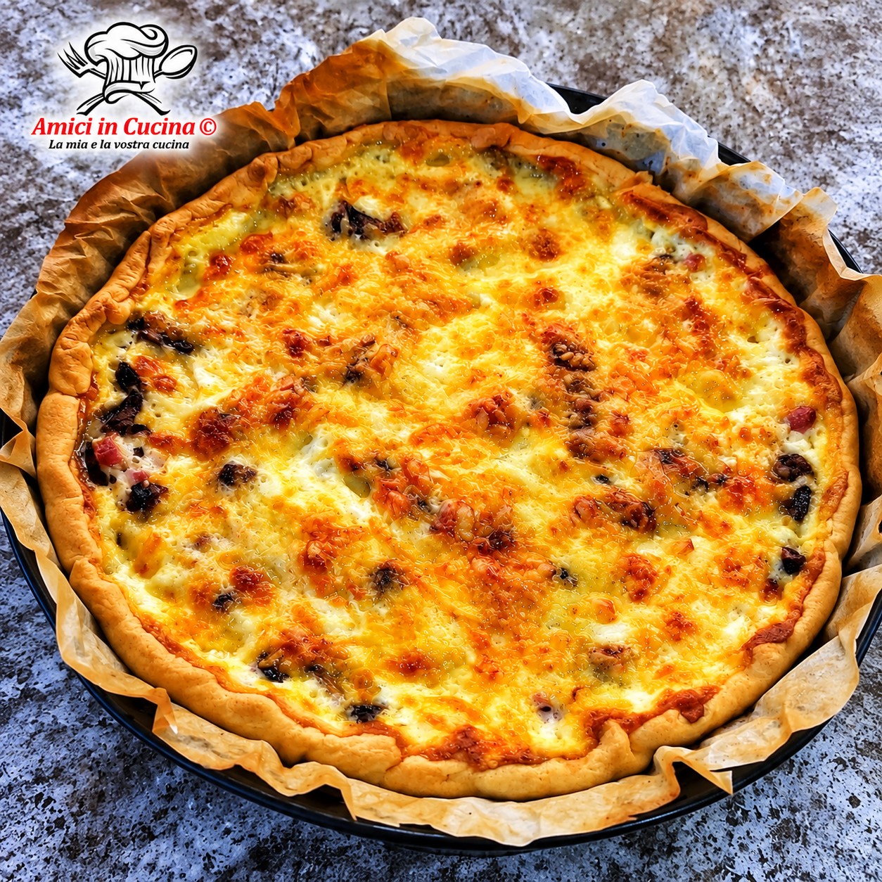Quiche Lorraine appena sfornata, rotonda, con bordi di pasta dorati e una superficie gratinata ricca di formaggio fuso e pezzetti di pancetta