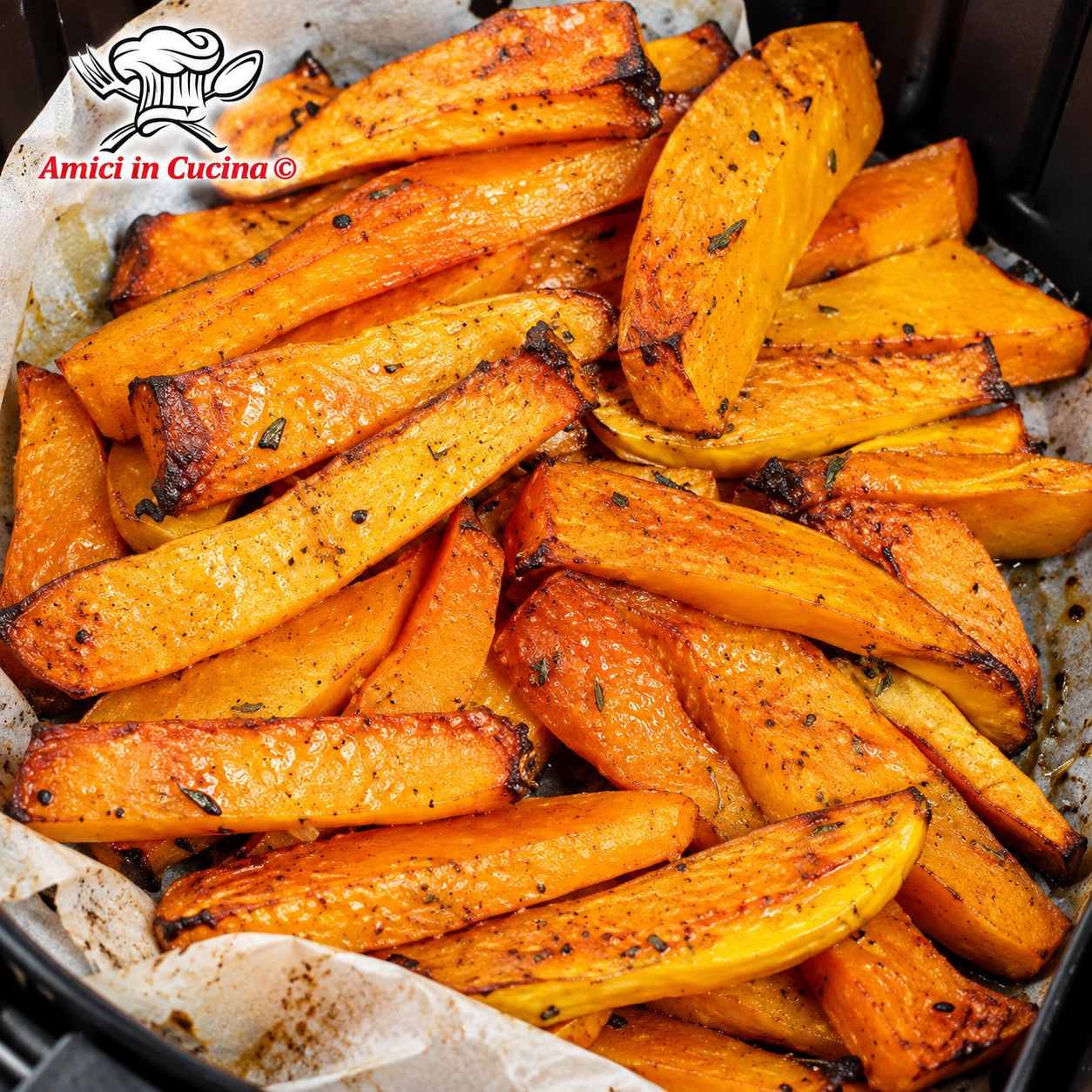 Ciotola di vetro con stick di zucca croccanti cotti in friggitrice ad aria, conditi con erbe aromatiche.