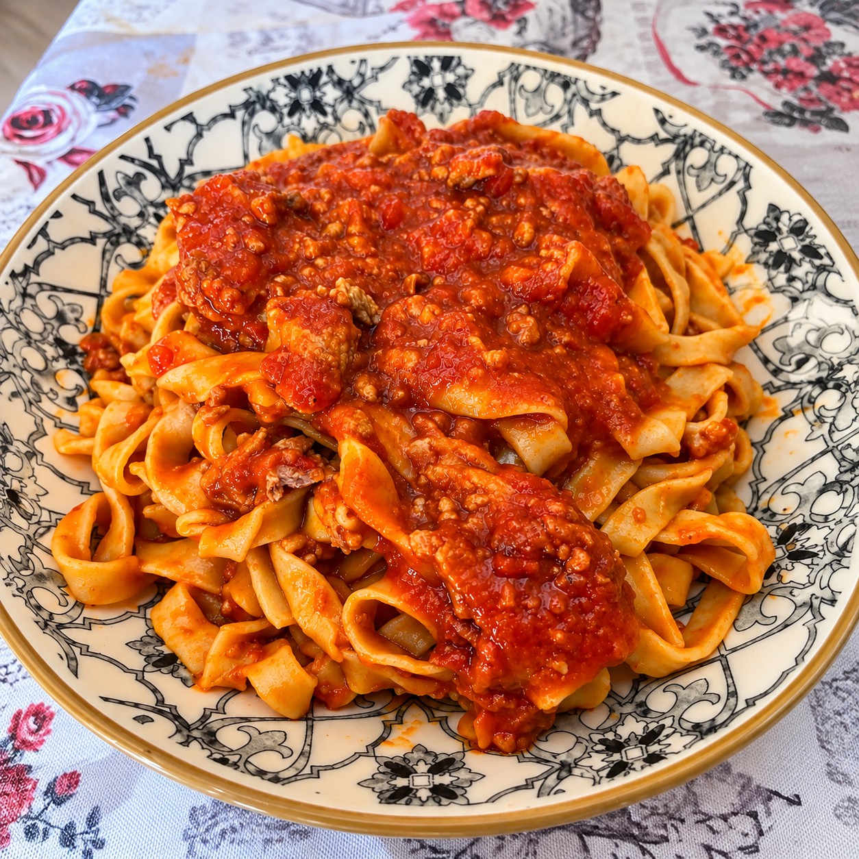 Piatto fondo decorato colmo di fettuccine all'uovo fatte in casa, condite con un ricco ragù di carne e una spolverata di parmigiano grattugiato