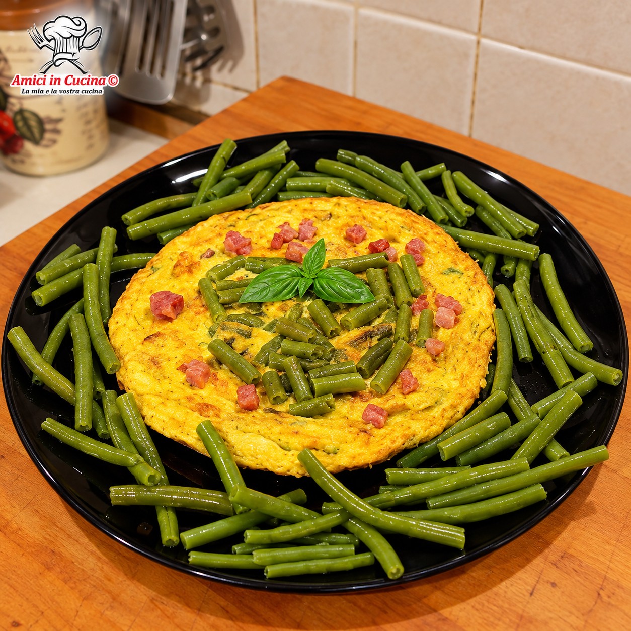 Frittata rotonda e dorata servita su un piatto nero, decorata con un cuore centrale di fagiolini verdi e cubetti di pancetta, circondata da fagiolini lessi
