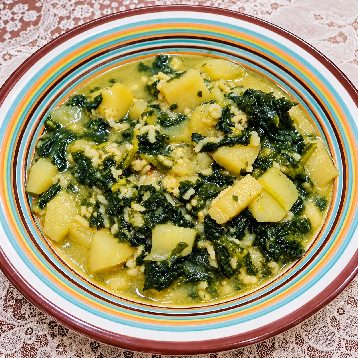 Piatto fondo colorato colmo di minestra calda a base di patate a cubetti, spinaci e pastina in un brodo leggero