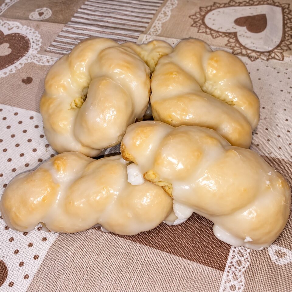Primo piano di taralli dolci siciliani a forma di ciambella intrecciata, ricoperti da una densa e lucida glassa bianca di zucchero e limone