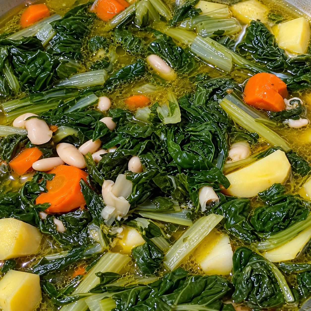 Pentola colma di zuppa fumante e brodosa con foglie di bietola, patate a tocchetti, fagioli bianchi e carot