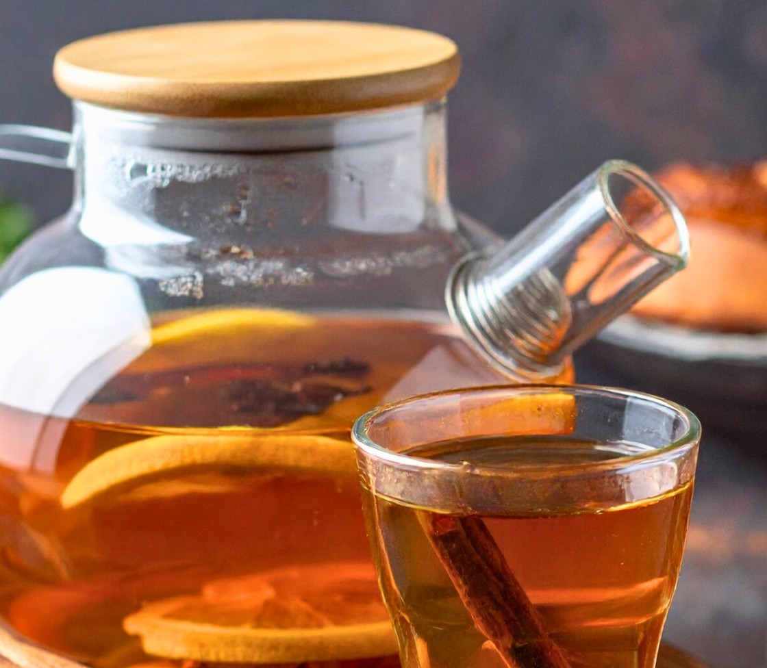 Tisana speziata in una teiera di vetro con un bicchiere pieno e dentro una stecca di cannella