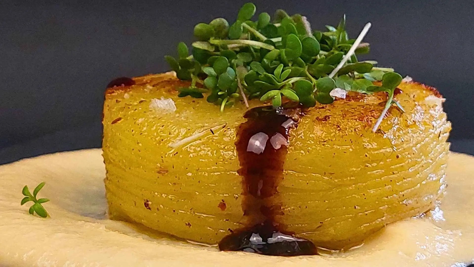 Disco di patata fondente su una crema di porro caramellato, una colata di glassa di aceto balsamico e sopra dei microgreens
