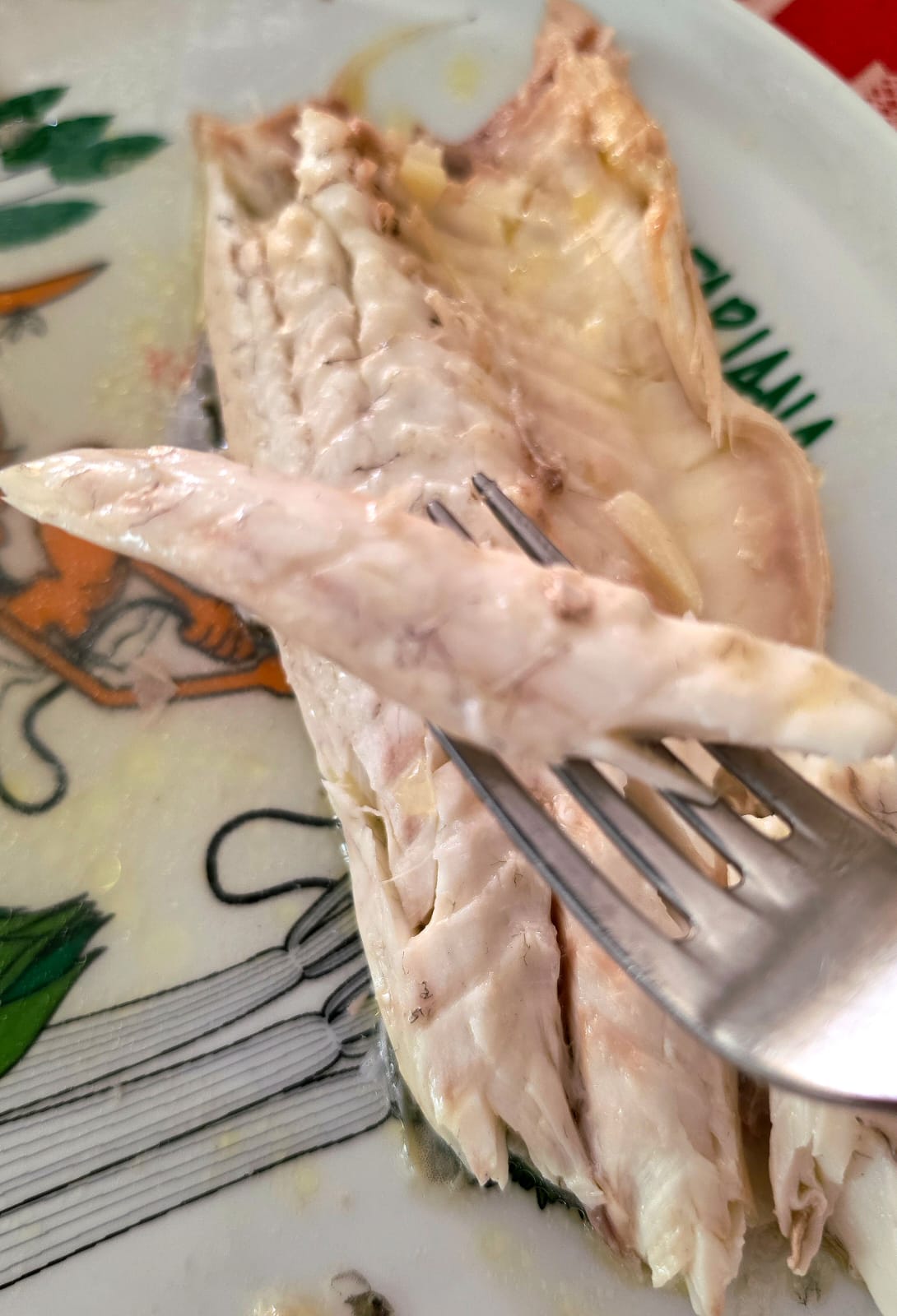 Filetto di branzino aglio e prezzemolo cotto in padella sollevato con una forchetta.