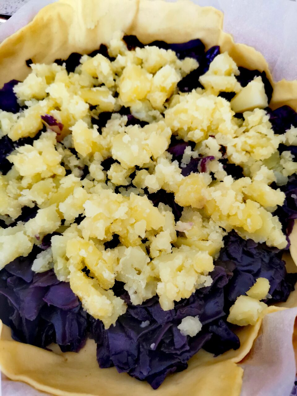 Torta salata cruda in teglia con guscio di pasta matta farcito con strati di cavolo viola e patate schiacciate prima della cottura
