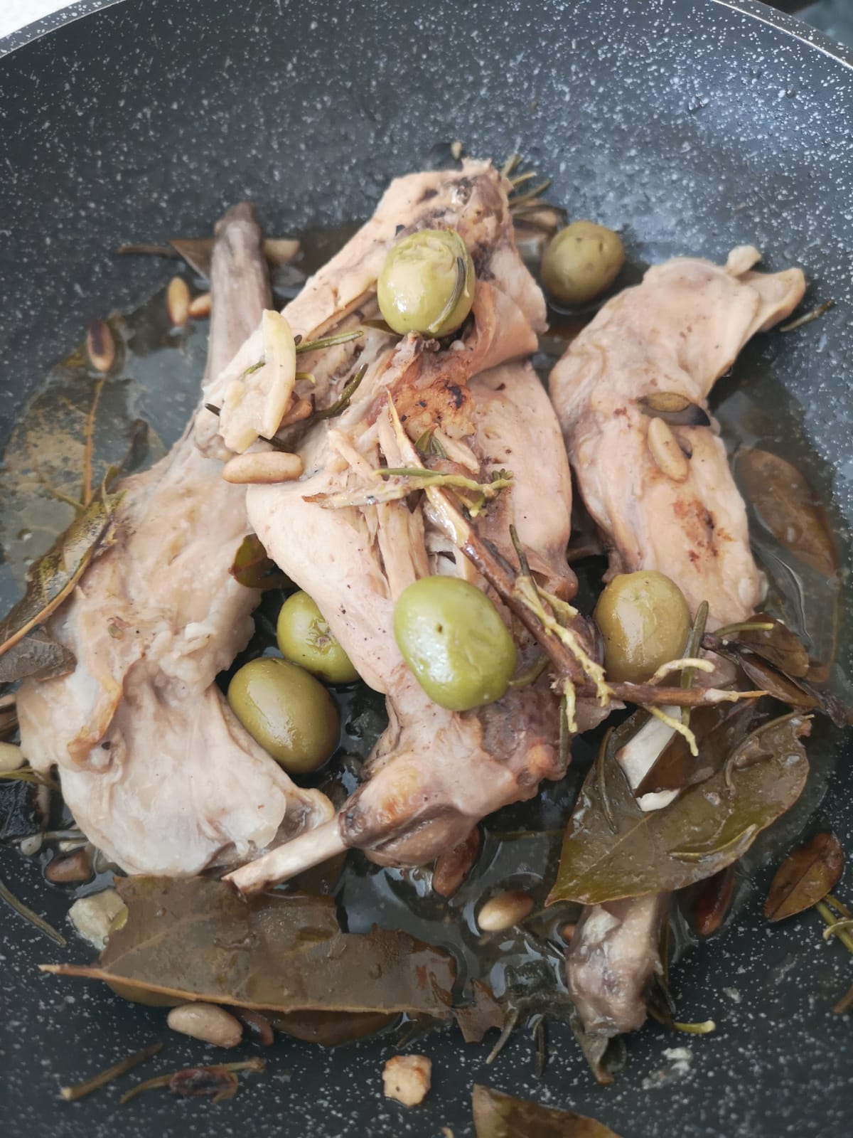 Coniglio alle erbe aromatiche cotto in padella con olive e pinoli