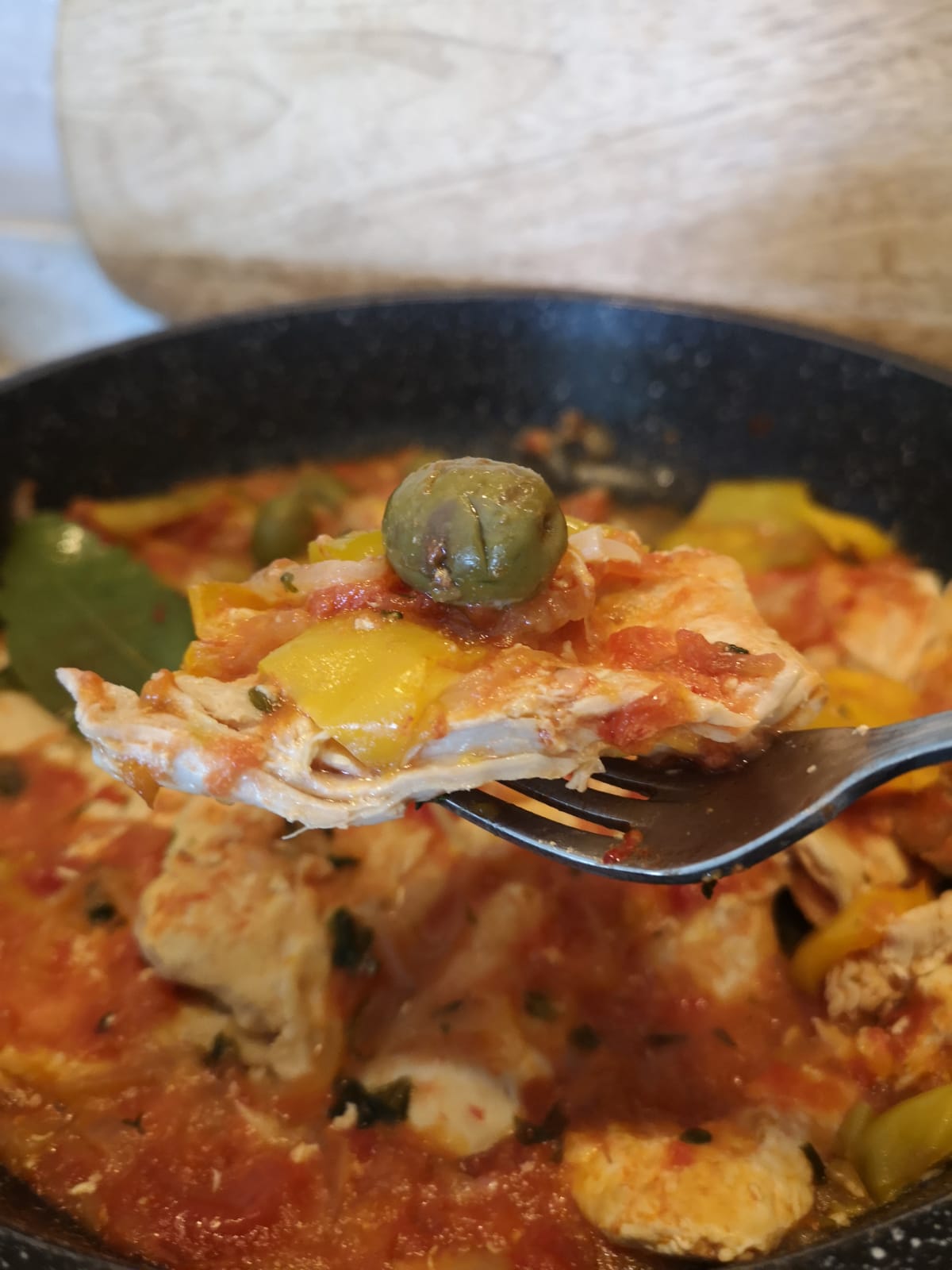 Un boccone di tenera fettina di tacchino ai peperoni gialli infilzato su una forchetta e completato da un'oliva verde.