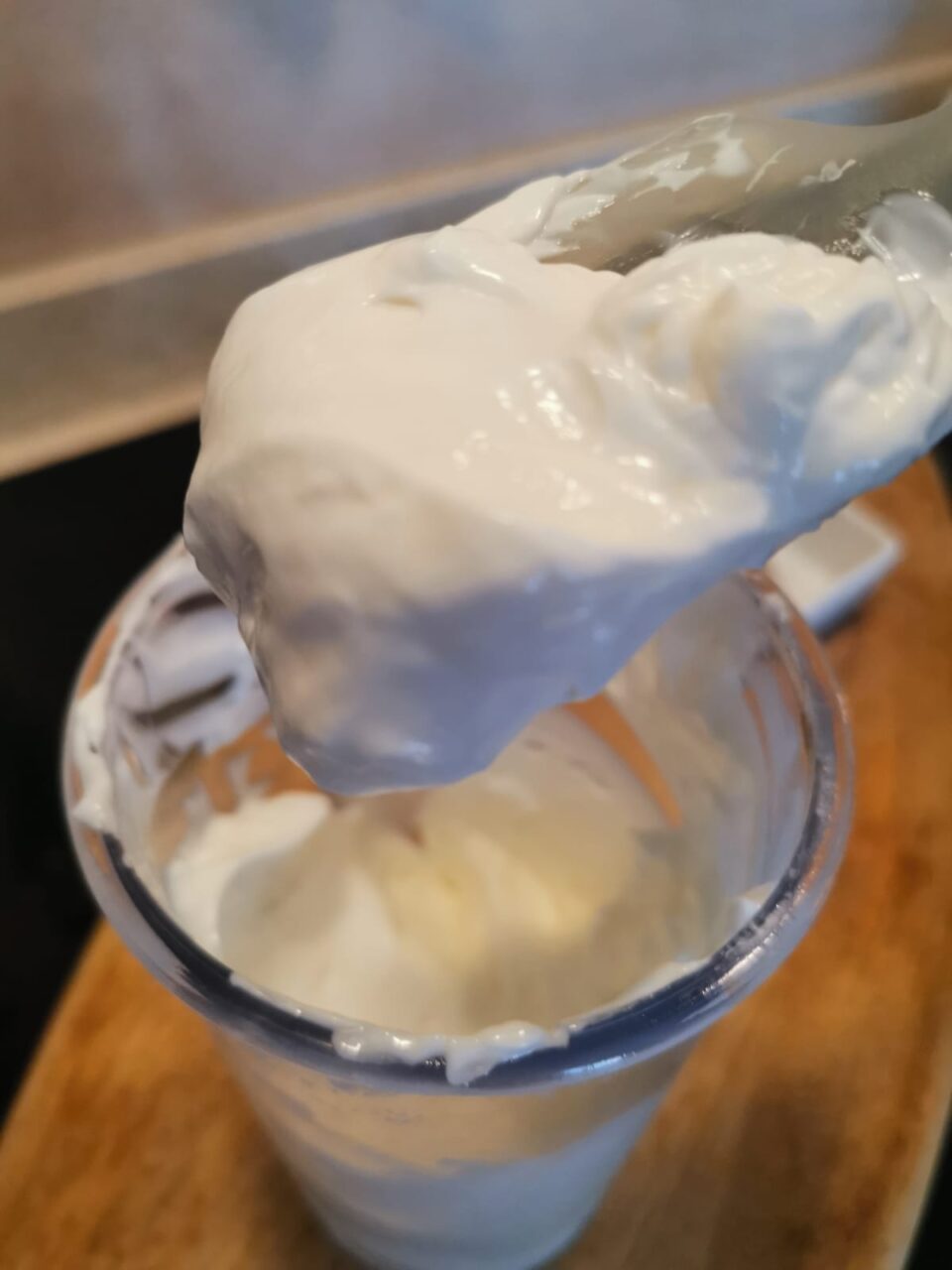 Una spatola da cucina solleva una cucchiaiata densa e compatta di maionese allo skyr dal bicchiere del minipimer