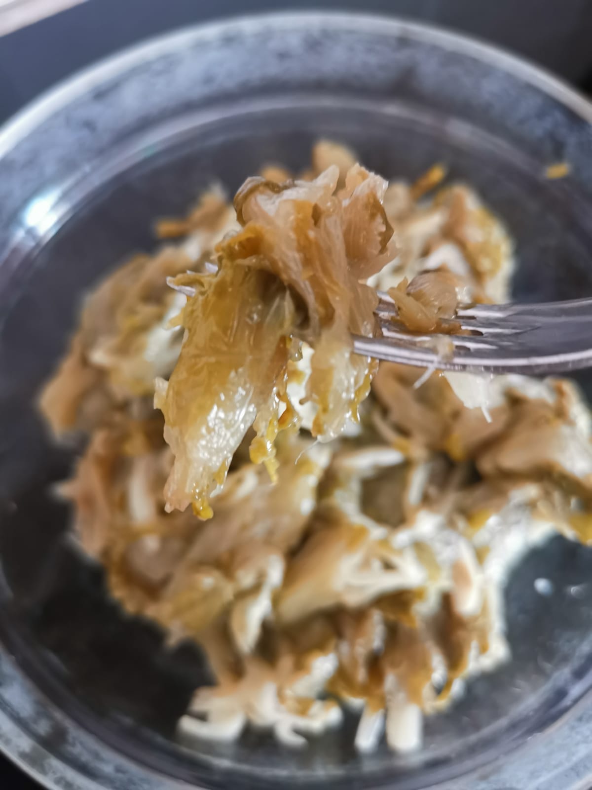 Un primo piano di una forchetta che solleva una porzione densa, cremosa e caramellata di scarola stufata da una ciotola di vetro.