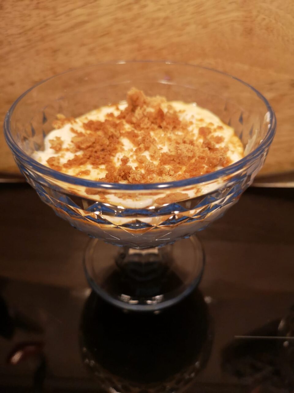 Vista dall'alto di una coppetta di vetro riempita con finto tiramisù light, decorata in superficie con caffè e frollini artigianali sbriciolati finemente.