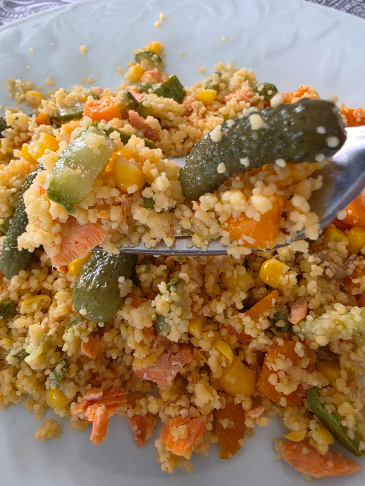 Boccone di couscous di legumi senza glutine con salmone, mais e cetriolino croccante su una forchetta.