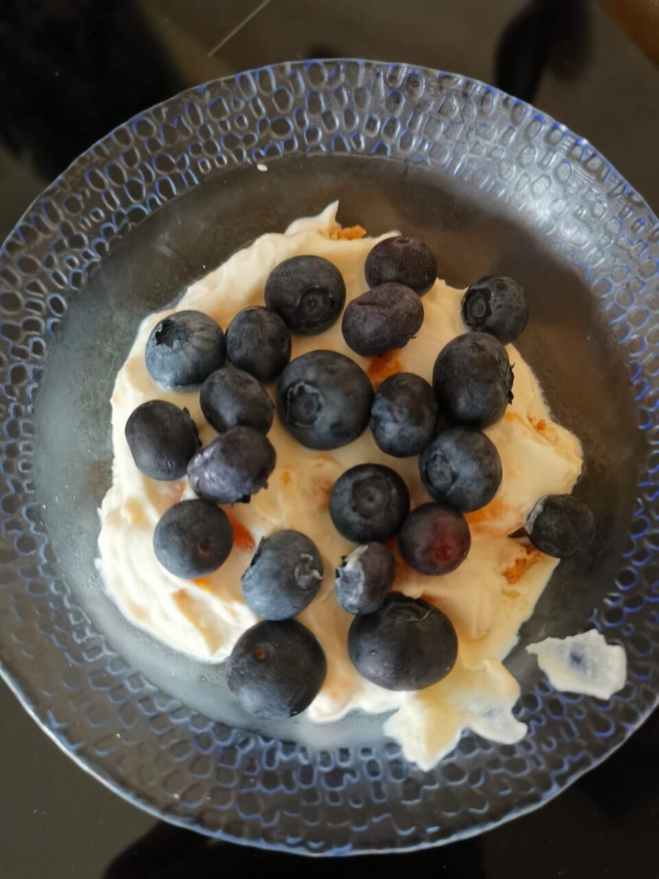 Veduta dall'alto di una coppetta trasparente con crema di ricotta liscia, ricoperta interamente da una cascata di mirtilli freschi e scuri.