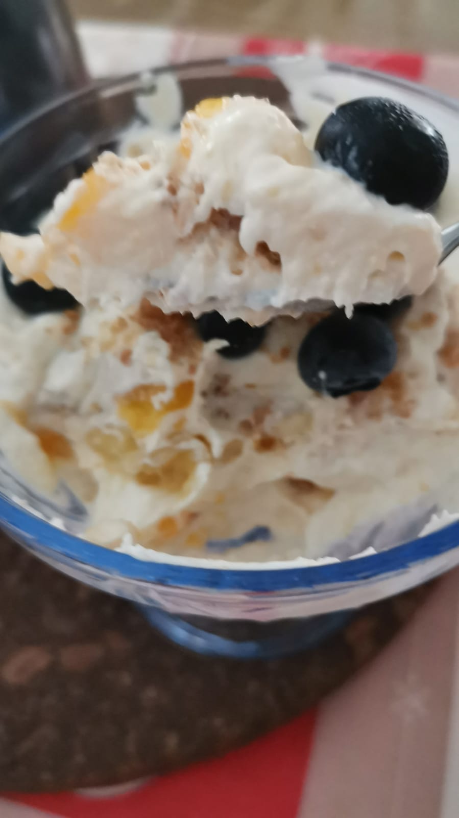Un cucchiaio raccoglie una porzione cremosa di dolce alla ricotta veloce in coppetta con mirtilli freschi e pezzetti di pesca nettarina.