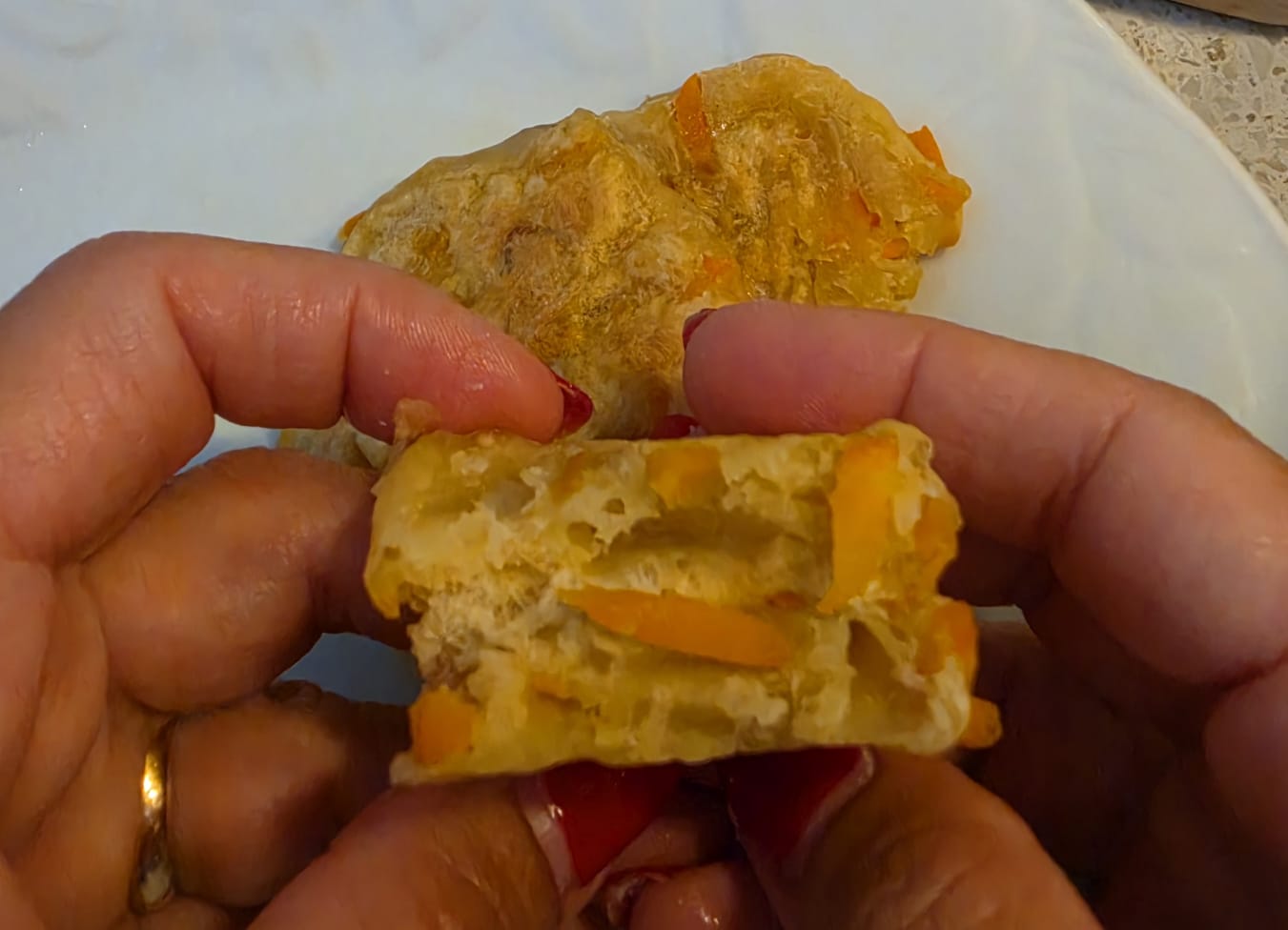 Mani che spezzano a metà una focaccina dorata di carote e cipolla di Tropea mostrando la consistenza morbida interna