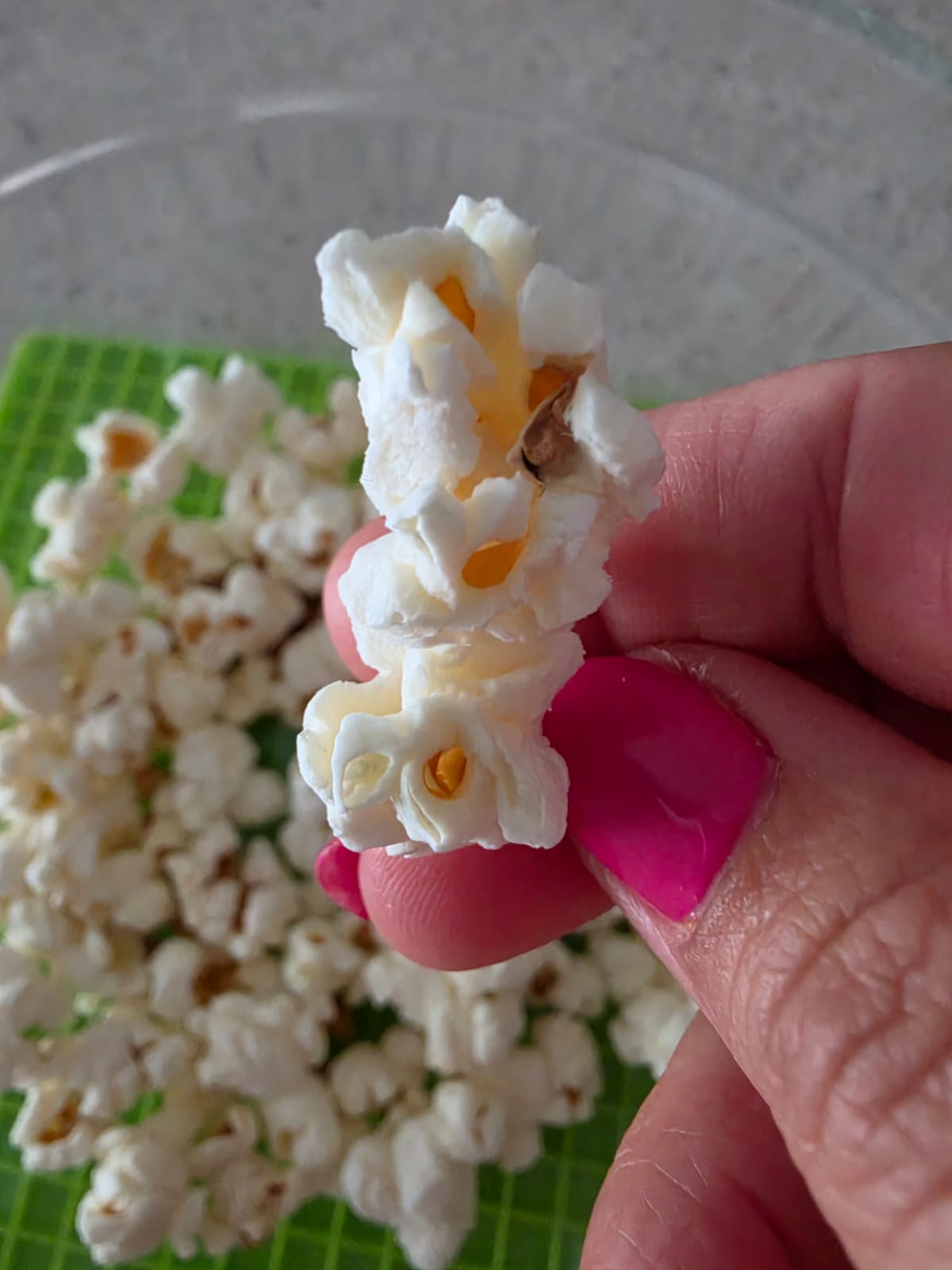 Primo piano di un popcorn bianco fatto al microonde senza olio tenuto tra le dita.