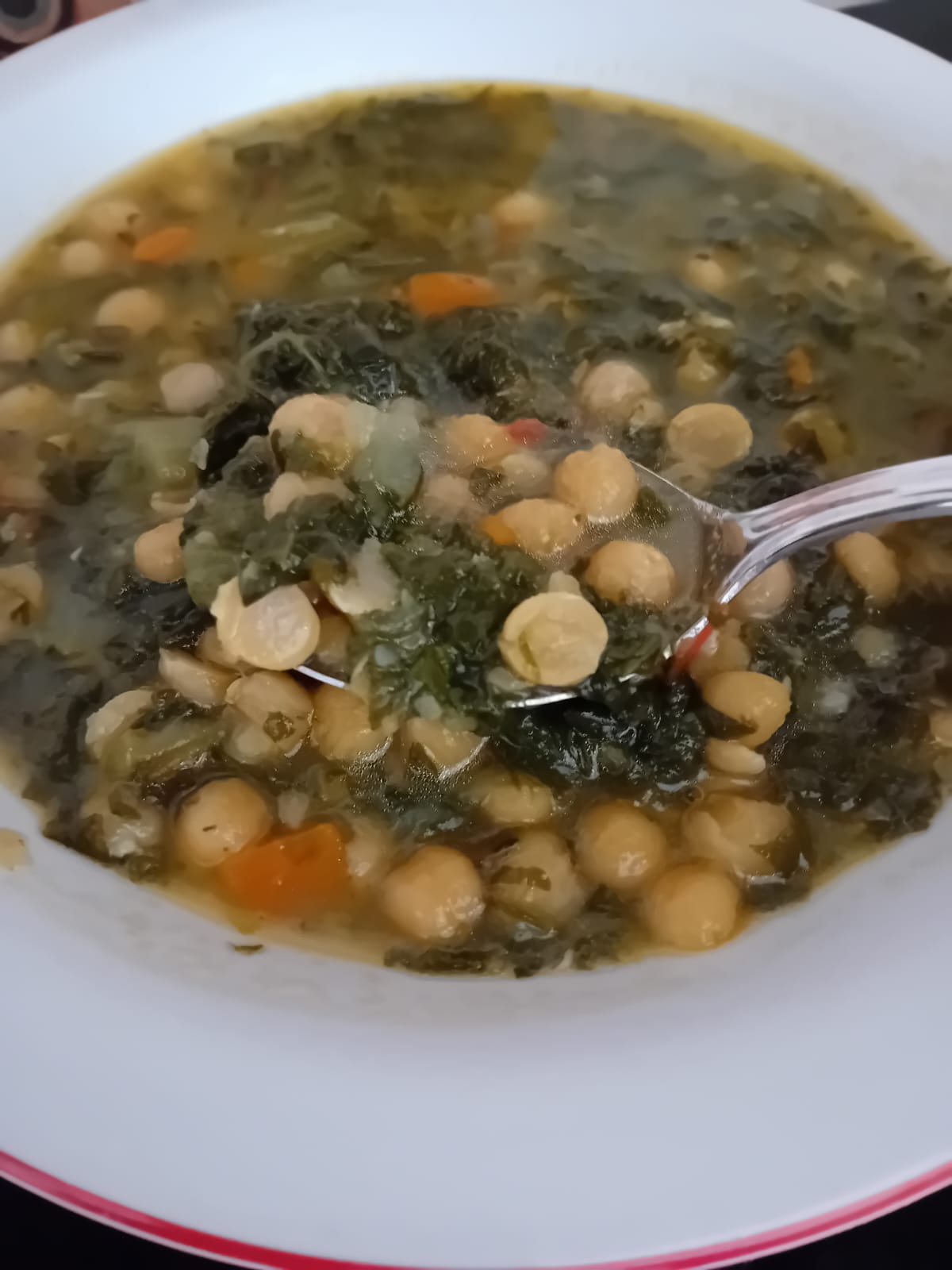 Primo piano di un piatto di zuppa estiva tiepida di ceci, bietole e carote servita con un cucchiaio