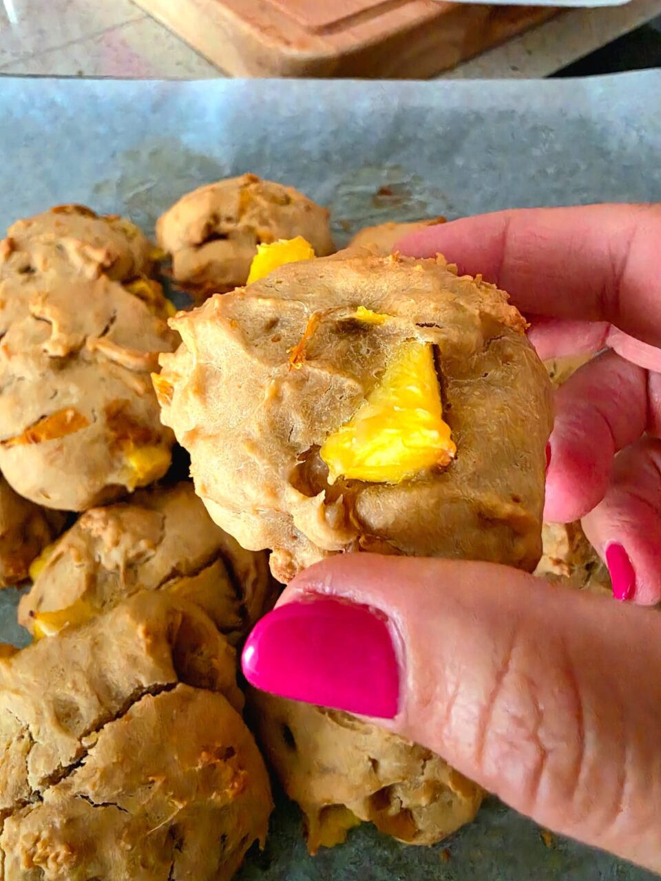 Un biscotto morbido alle prugne gialle dorato e rustico tenuto in mano, con pezzi di frutta fresca ben visibili sulla superficie.