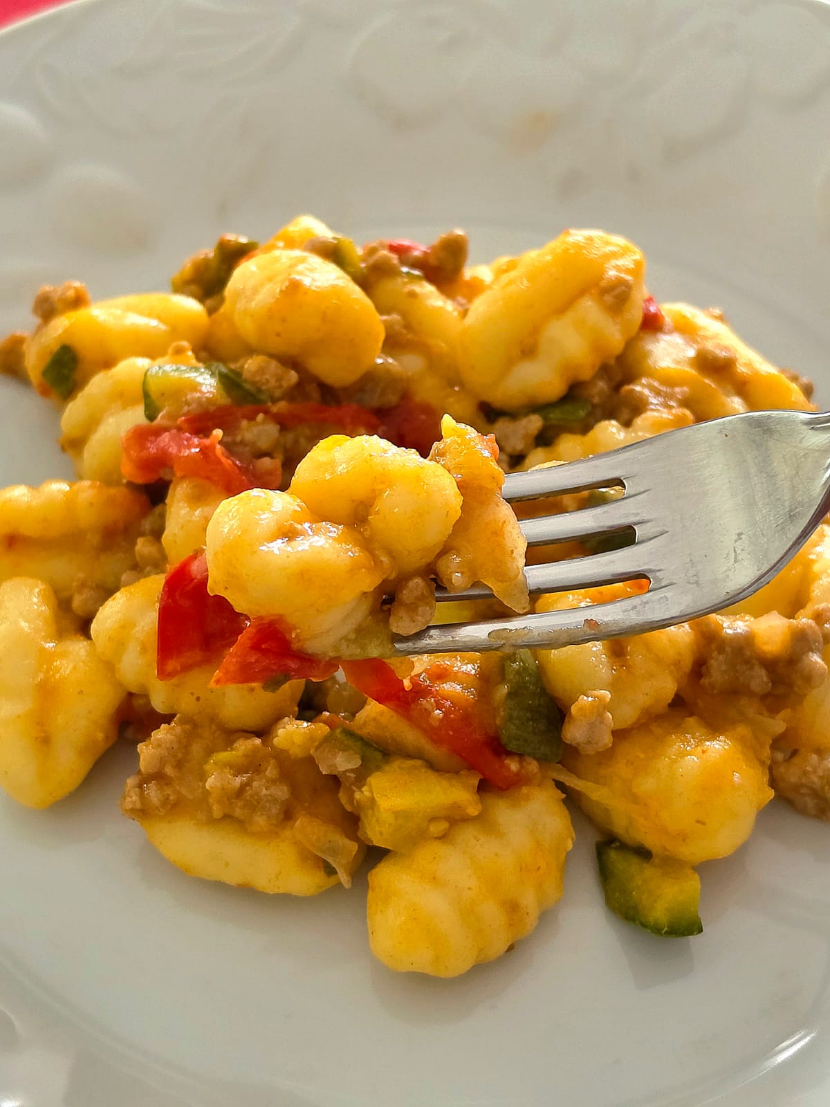 Piatto di gnocchi di patate conditi con ragù leggero di tacchino, zucchine e pomodorini alla paprika con una forchetta in primo piano.