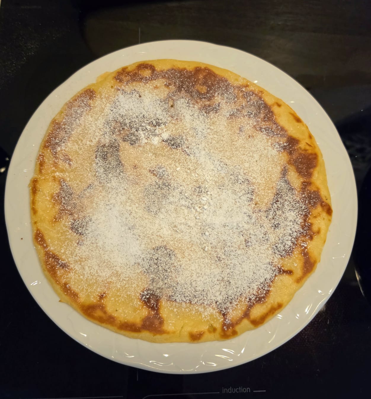 Un maxi pancake in padella intero e soffice su un piatto, spolverato con zucchero a velo.