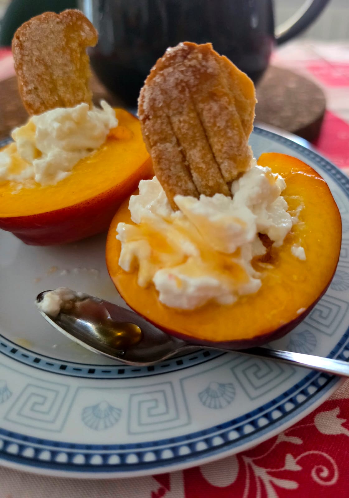 Mezze pesche nettarine ripiene con crema di ricotta e panna, guarnite con colata di miele e un biscotto croccante.