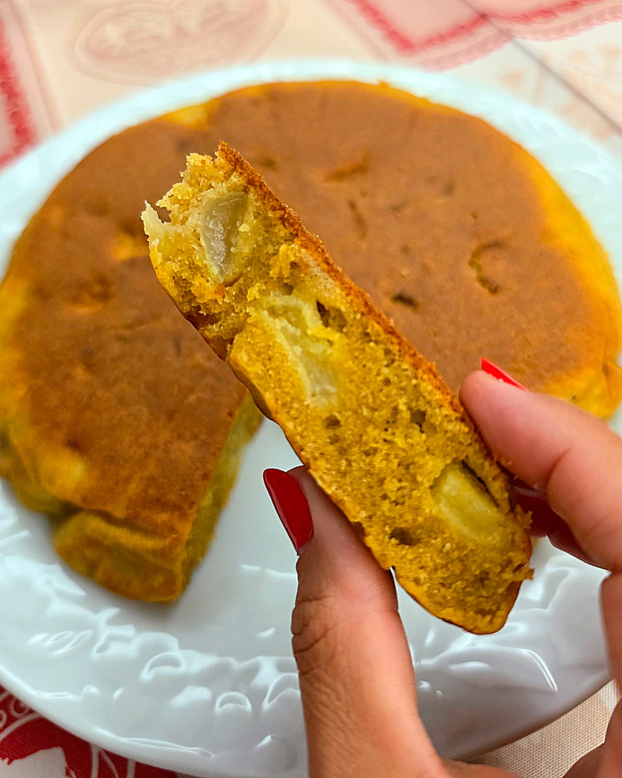 Fetta di torta in padella alle mele e uva tenuta in mano che mostra l'interno soffice con pezzetti di frutta.