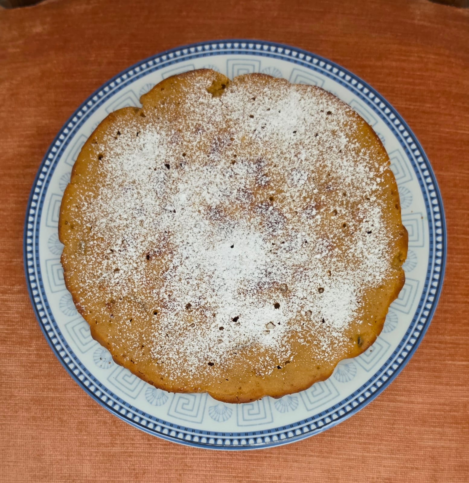 Vista dall'alto di una torta in padella soffice e tonda all'uvetta, spolverata di zucchero a velo, su un piatto decorato.