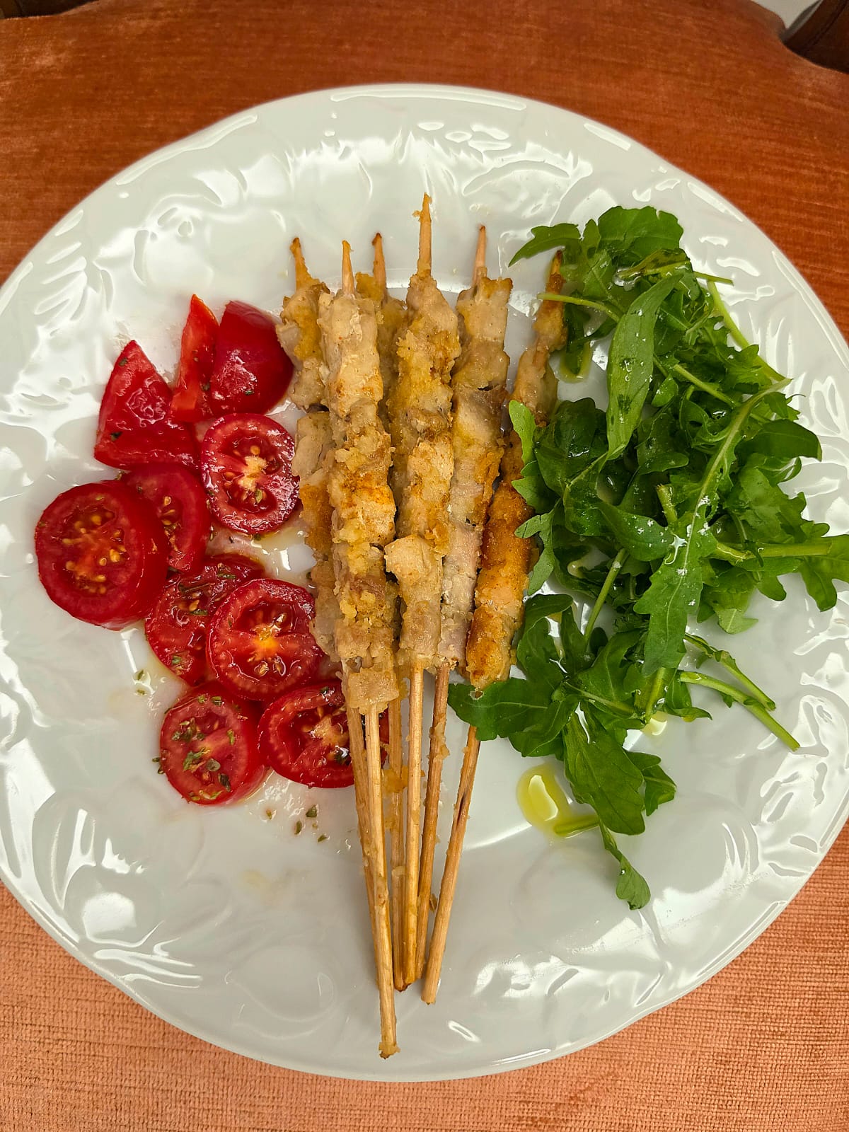 Arrosticini di tacchino e pancetta in padella serviti in un piatto bianco con rucola fresca e pomodorini