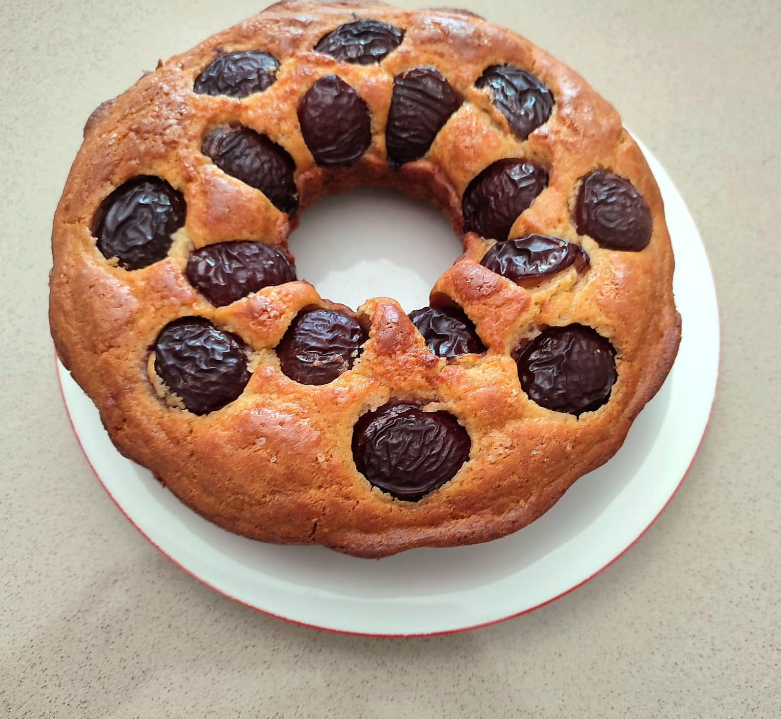 Ciambella soffice alle prugne e skyr dorata e decorata con prugne fresche in superficie.