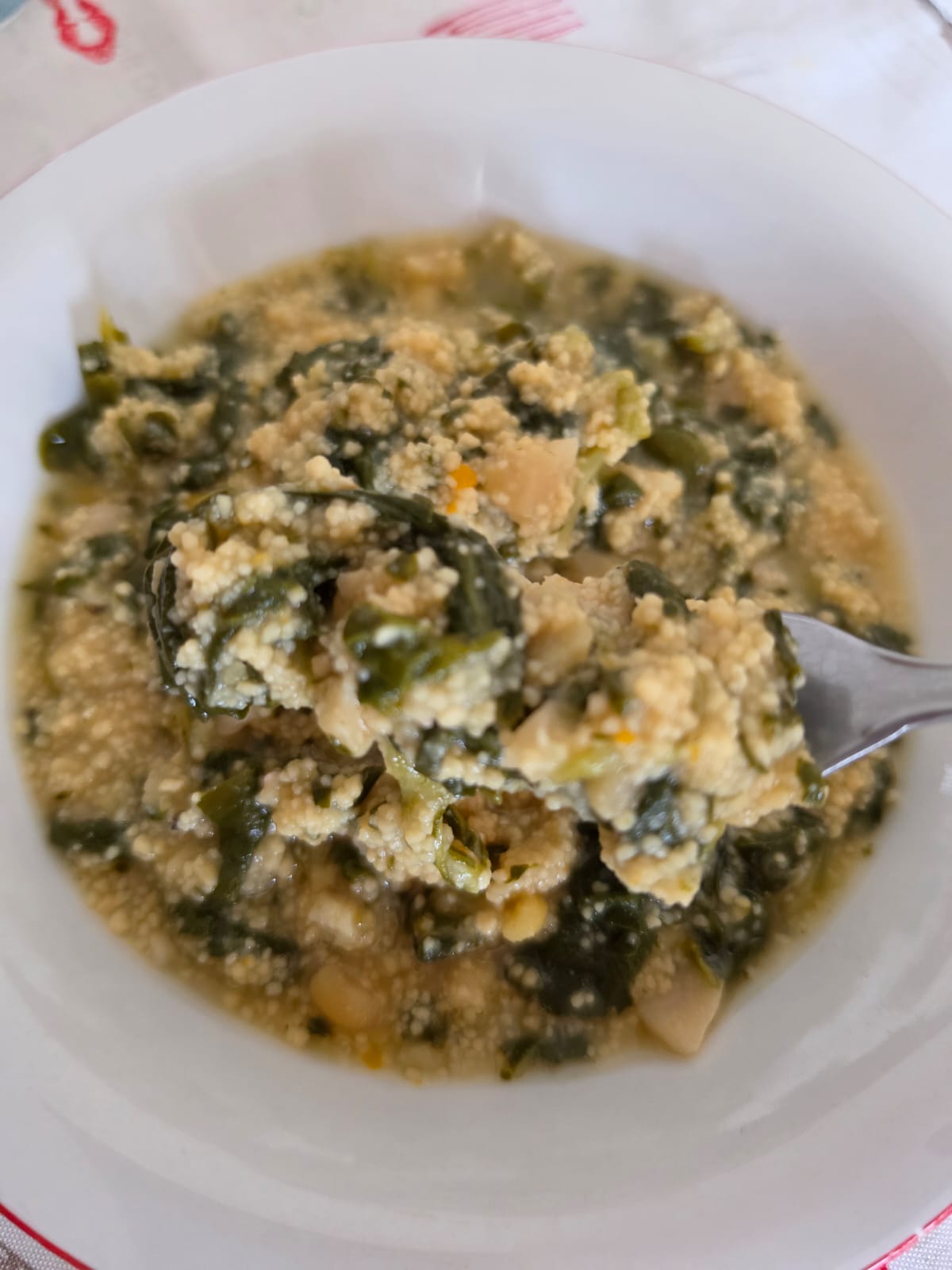 Primo piano di una porzione di couscous cremoso con bietole e ceci raccolto con una forchetta.