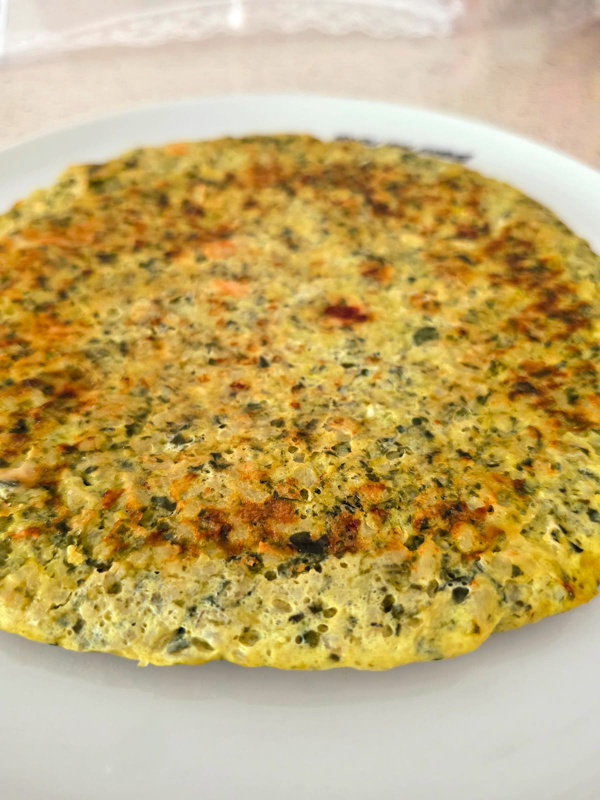 Frittata con risotto avanzato agli spinaci e bietole dorata in padella servita su un piatto bianco