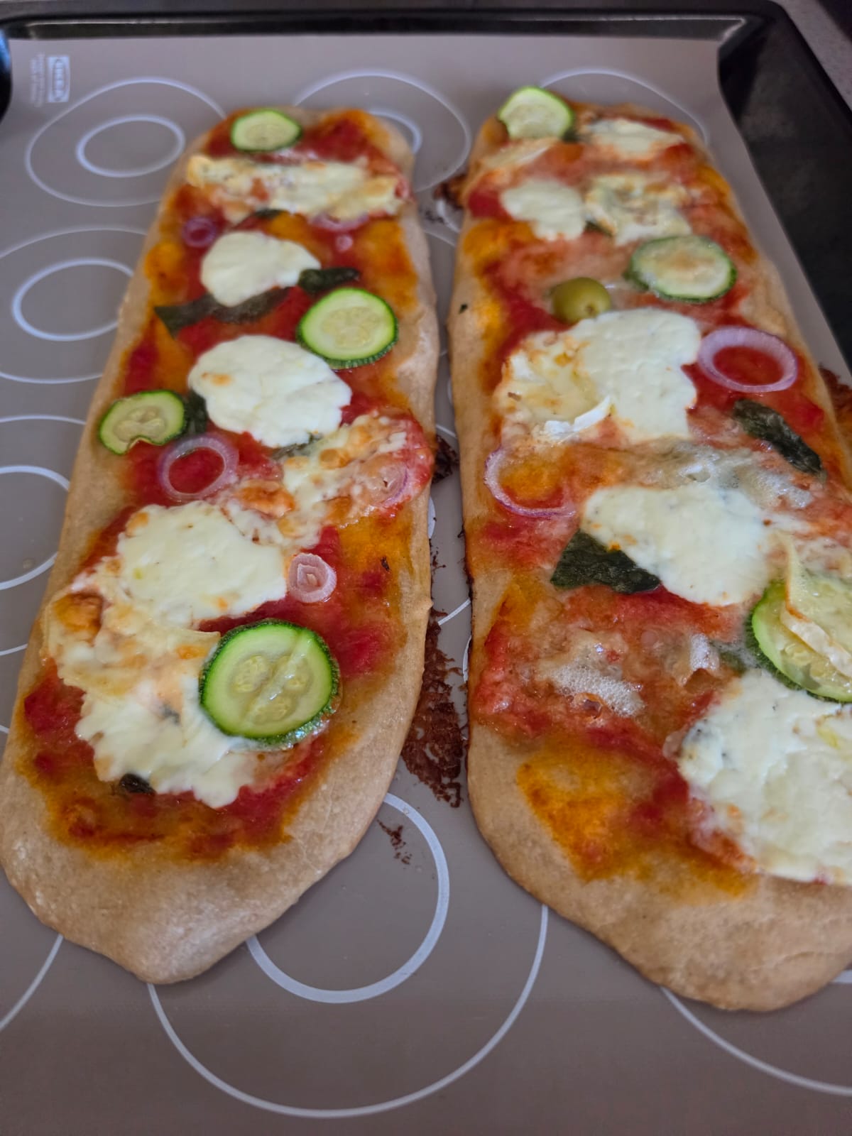 Due lingue di pizza soffici cotte al forno e condite con pomodoro, stracchino, gorgonzola, zucchine e cipolla disposte sulla teglia