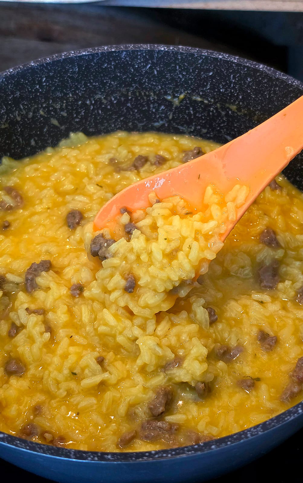 Risotto allo zafferano con carne macinata di manzo cremoso servito in pentola con un cucchiaio