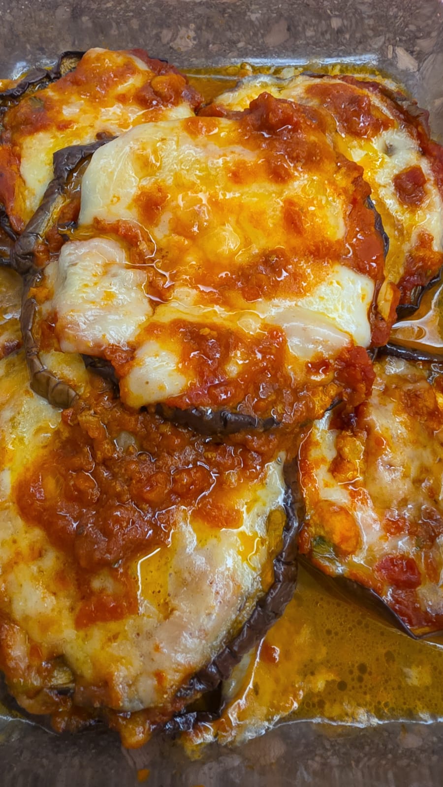 Pirofila in vetro con melanzane al forno condite con ragù di carne, pomodoro e provola filante ben dorata.