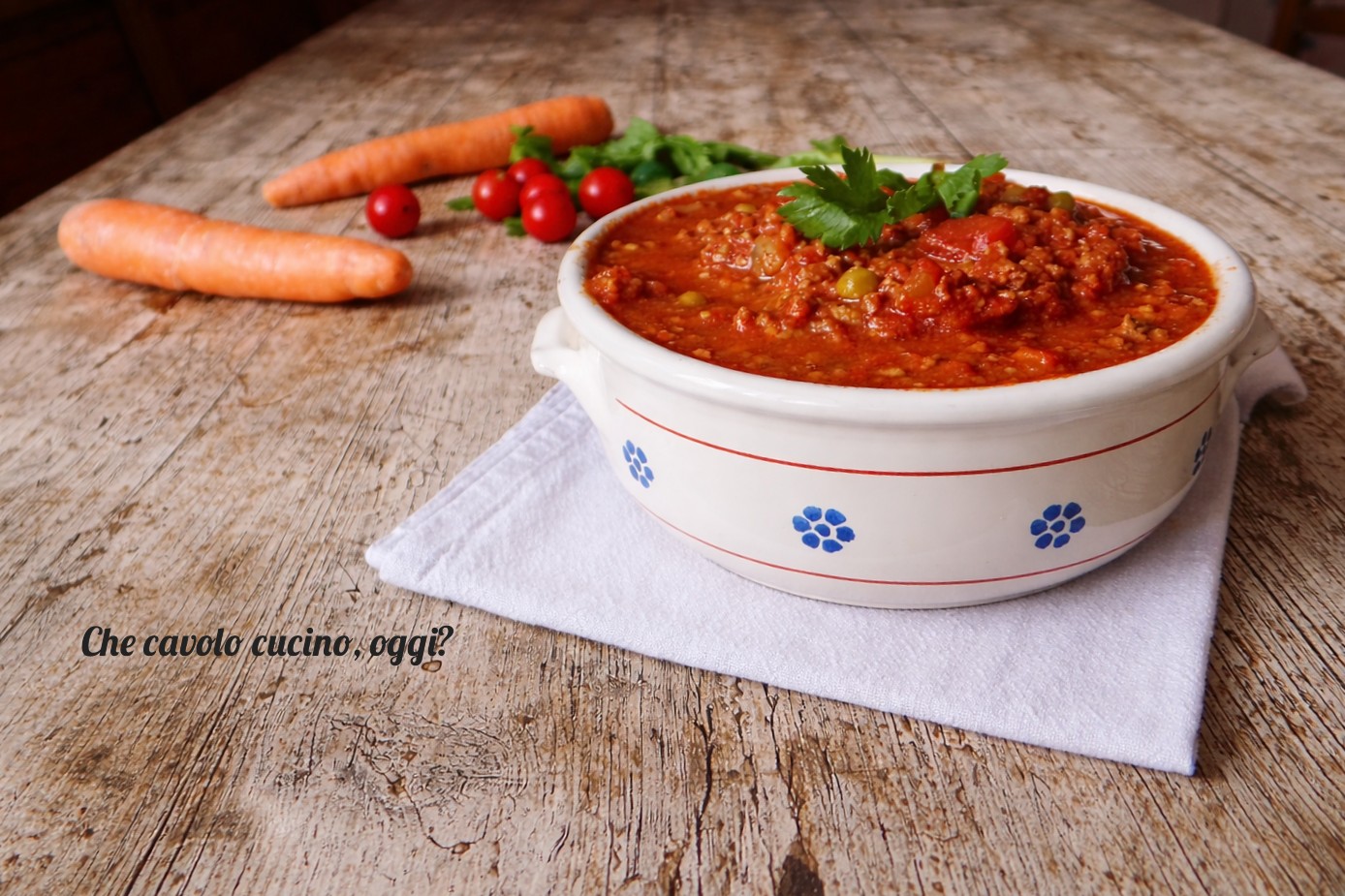 ragù di carne fatto in casa servito in ciotola con prezzemolo, carote e pomodorini sullo sfondo