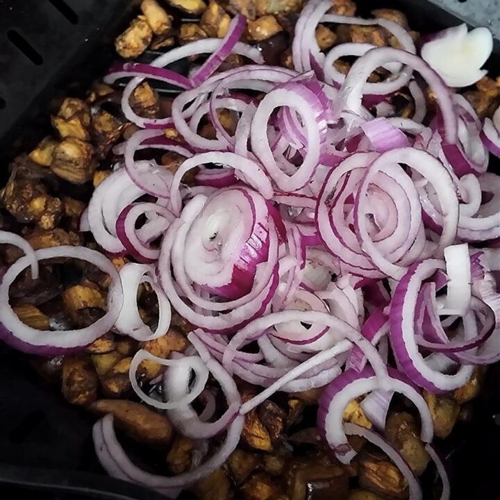 Nel fratte po prendi una cipolla di Tropea e puliscila dalla parte esterna secca poi tagliala a rondelle della stessa dimensione. Tienile da parte mentre le melanzane stanno cuocendo in friggitrice ad aria.