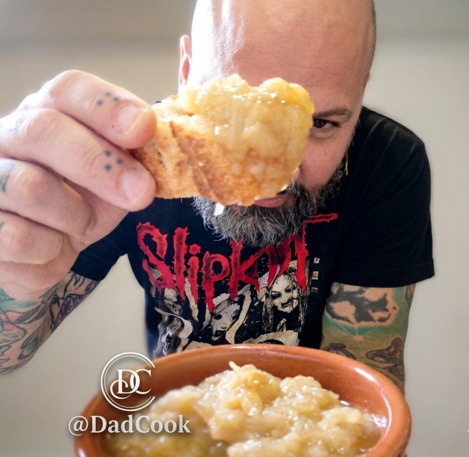 Primo piano di una fetta di pane croccante con sopra abbondante cipolla caramellata, tenuta in mano dall'autore del blog durante l'assaggio.