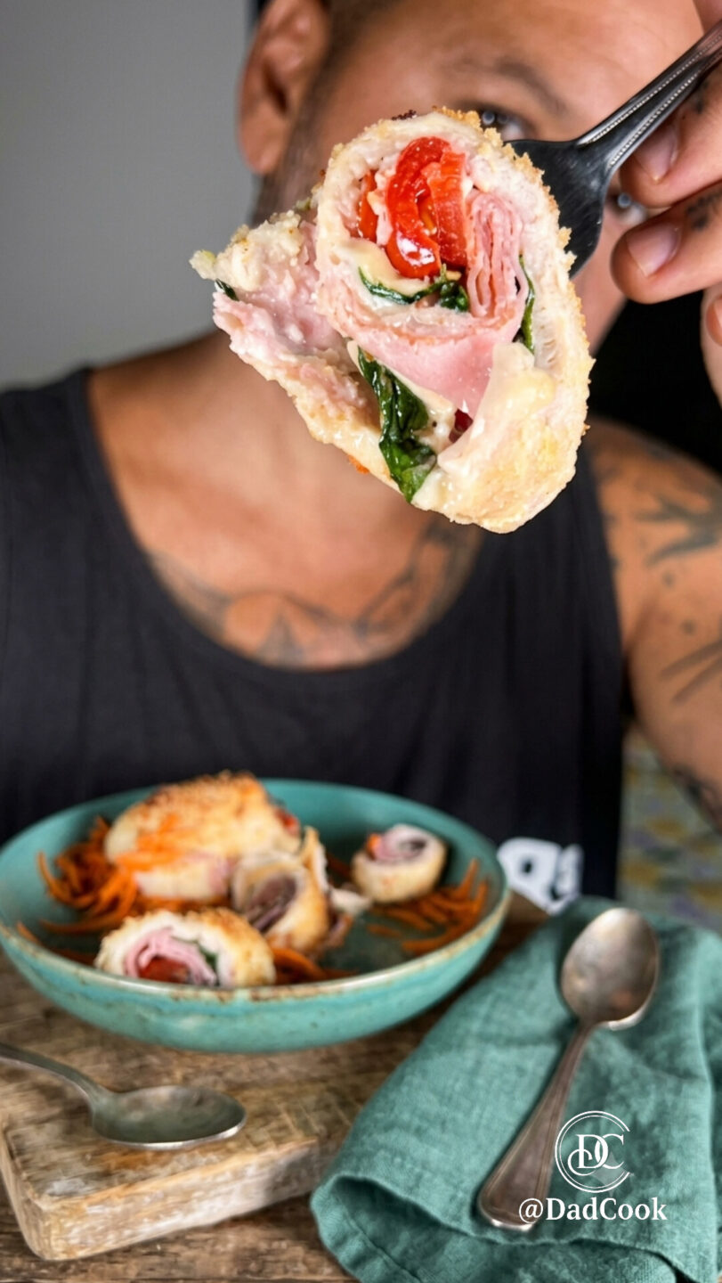 Un'immagine orizzontale e invitante di due ciotole blu acqua con involtini di pollo arrosto tagliati a metà e farciti, serviti su un letto di carote grattugiate e un tagliere di legno rotondo. Ci sono ciotole di menta fresca, carote grattugiate e pomodori freschi sullo sfondo, con posate di bronzo su un tovagliolo ocra in primo piano.