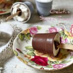 Gelatini al Cioccolato senza Zucchero su piattino elegante con decorazioni floreali, panna interna e stecco centrale in vista.