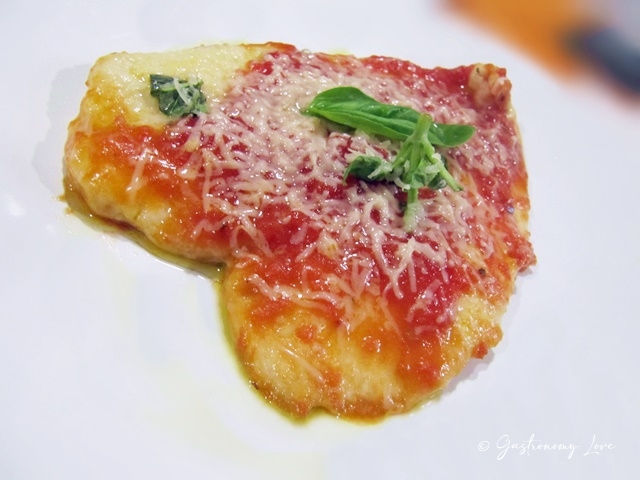 Piatto di scaloppine di petto di pollo al pomodoro e parmigiano filante guarnite con foglie di basilico fresco.