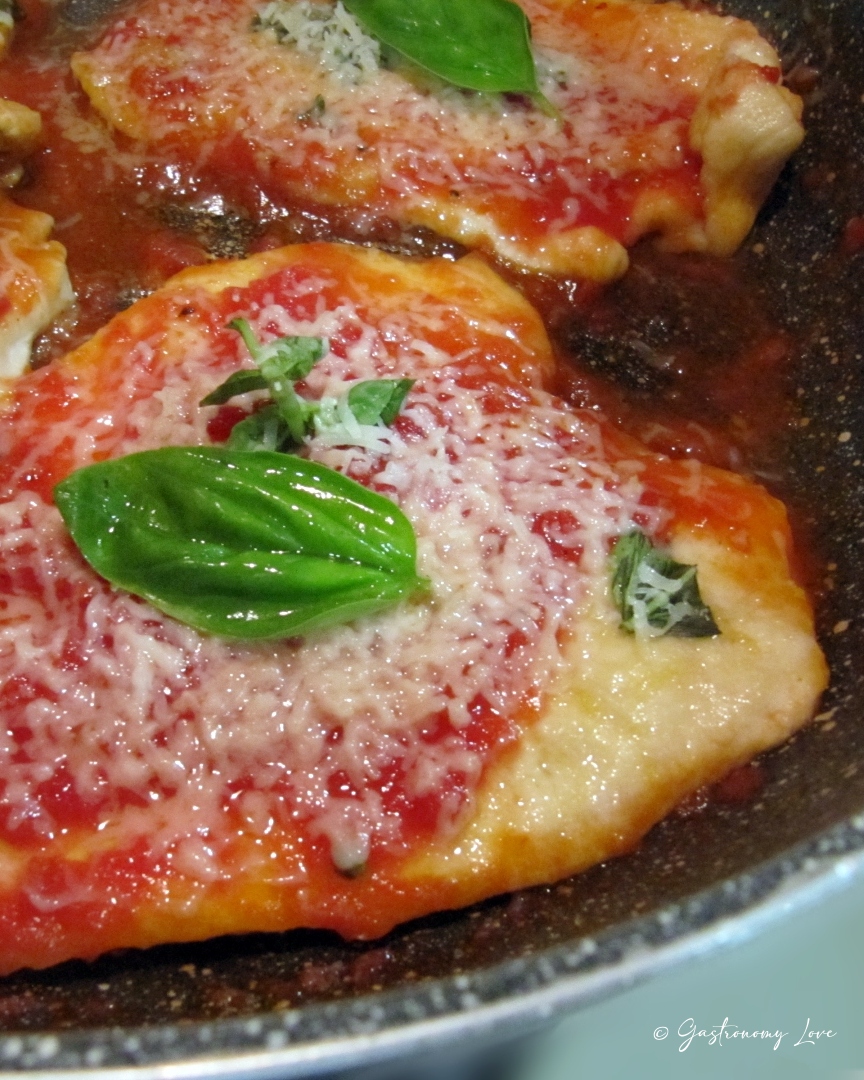 Fette di petto di pollo al pomodoro e parmigiano filante guarnite con basilico fresco in padella.