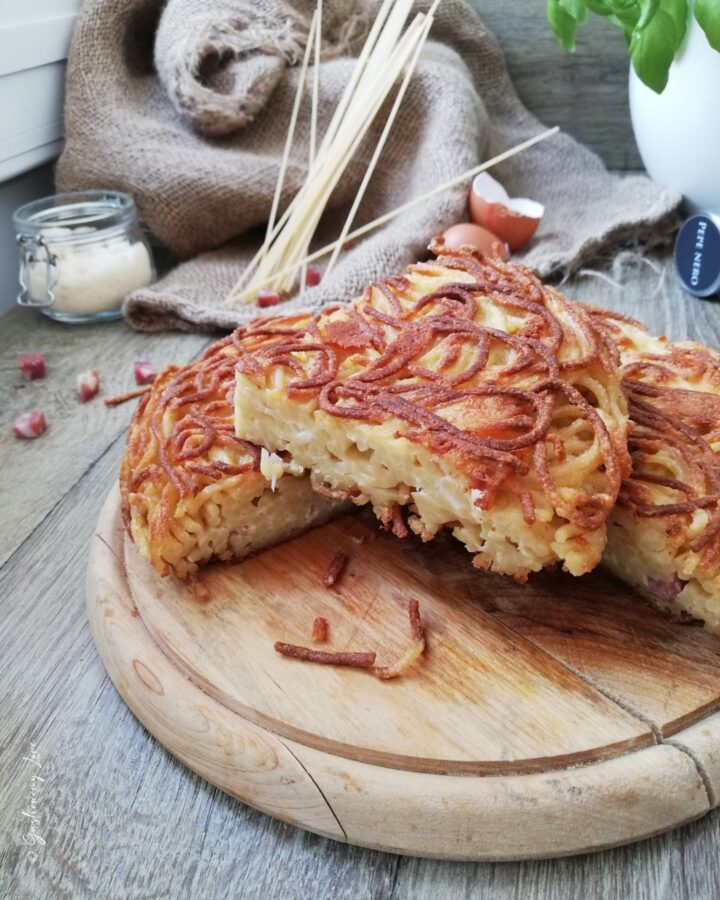 Fetta di frittata di spaghetti napoletana alta 4 cm con interno morbido farcito di salame e provola, crosticina dorata esterna, servita su tagliere di legno rustico.