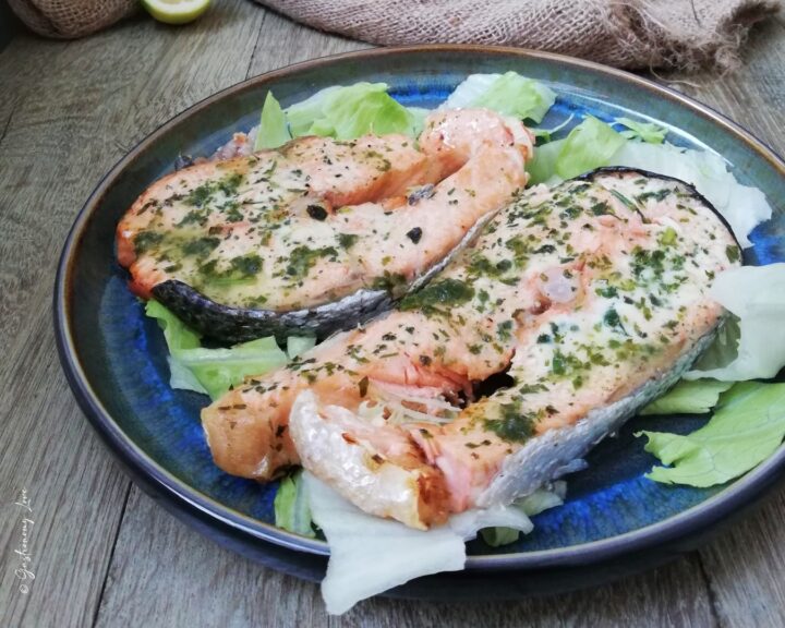 Tranci di salmone cotti in friggitrice ad aria conditi con salmoriglio di limone e prezzemolo su un piatto bianco.