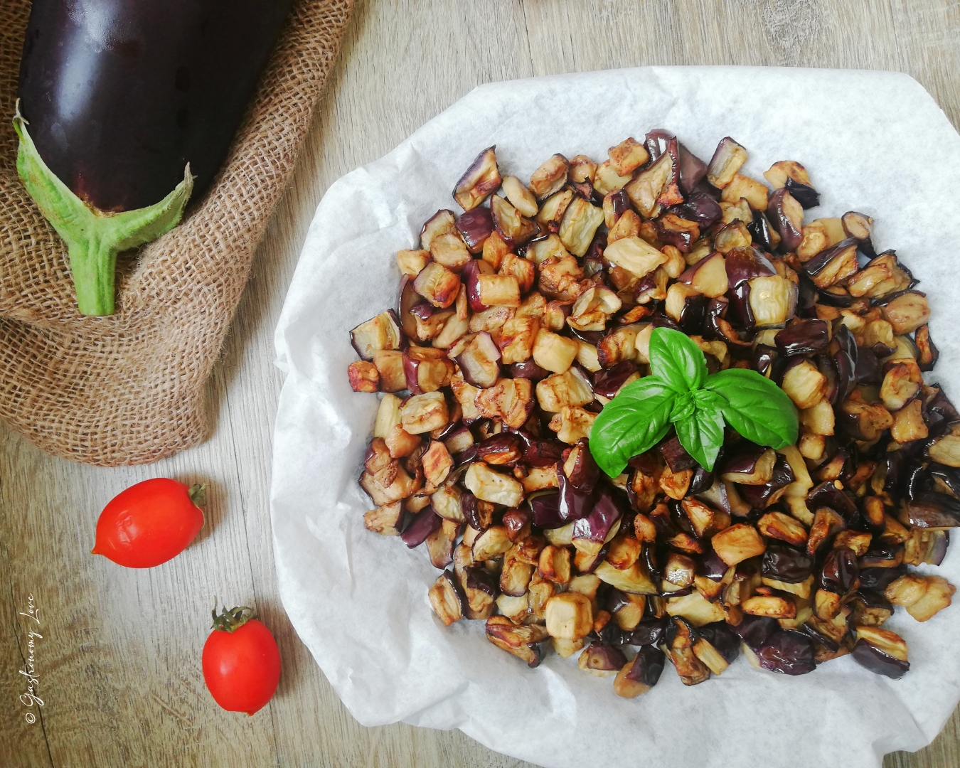 Melanzane a cubetti fritte in friggitrice ad aria disposte su carta forno con pomodorini e basilico freschi