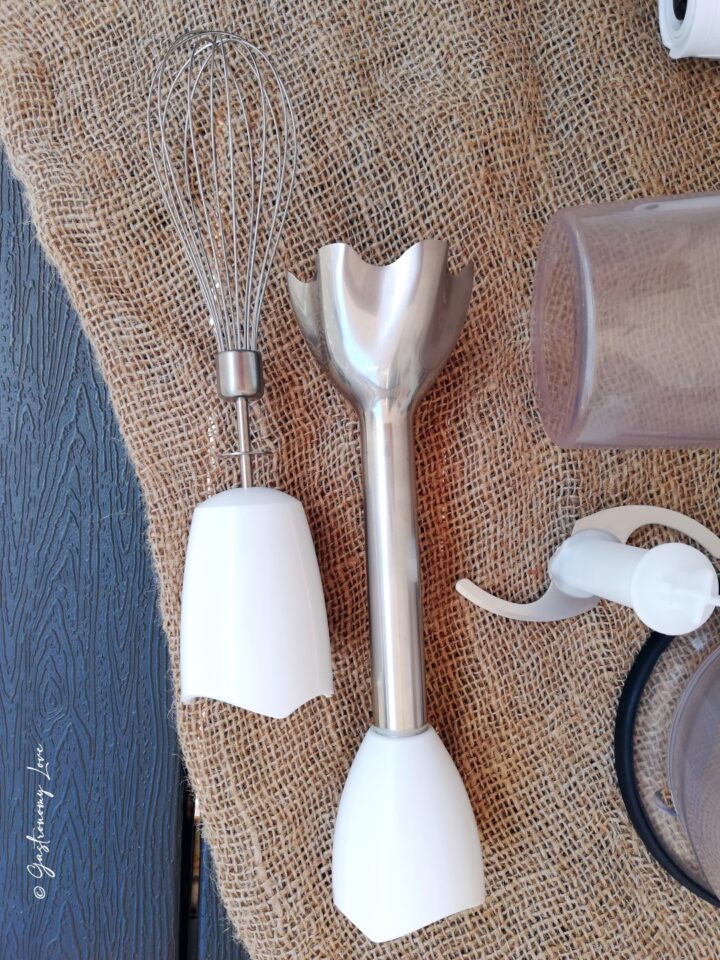 Accessori e fruste del minipimer multifunzione appoggiati su un piano in juta.
