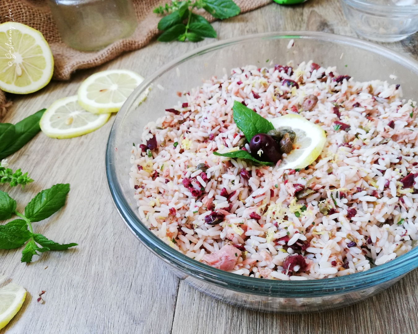 Inquadratura angolata della ciotola di riso freddo dove si notano i pezzettoni di tonno sott'olio, le olive sminuzzate e la citronette lucida che avvolge il piatto.