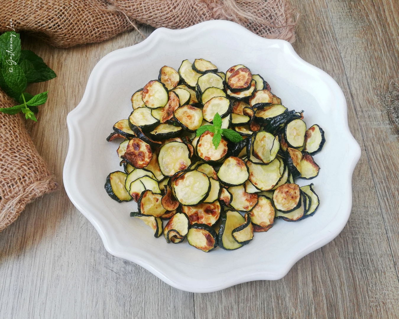 Zucchine a rondelle fritte in friggitrice ad aria dorate e croccanti in una ciotola bianca, decorate con menta fresca