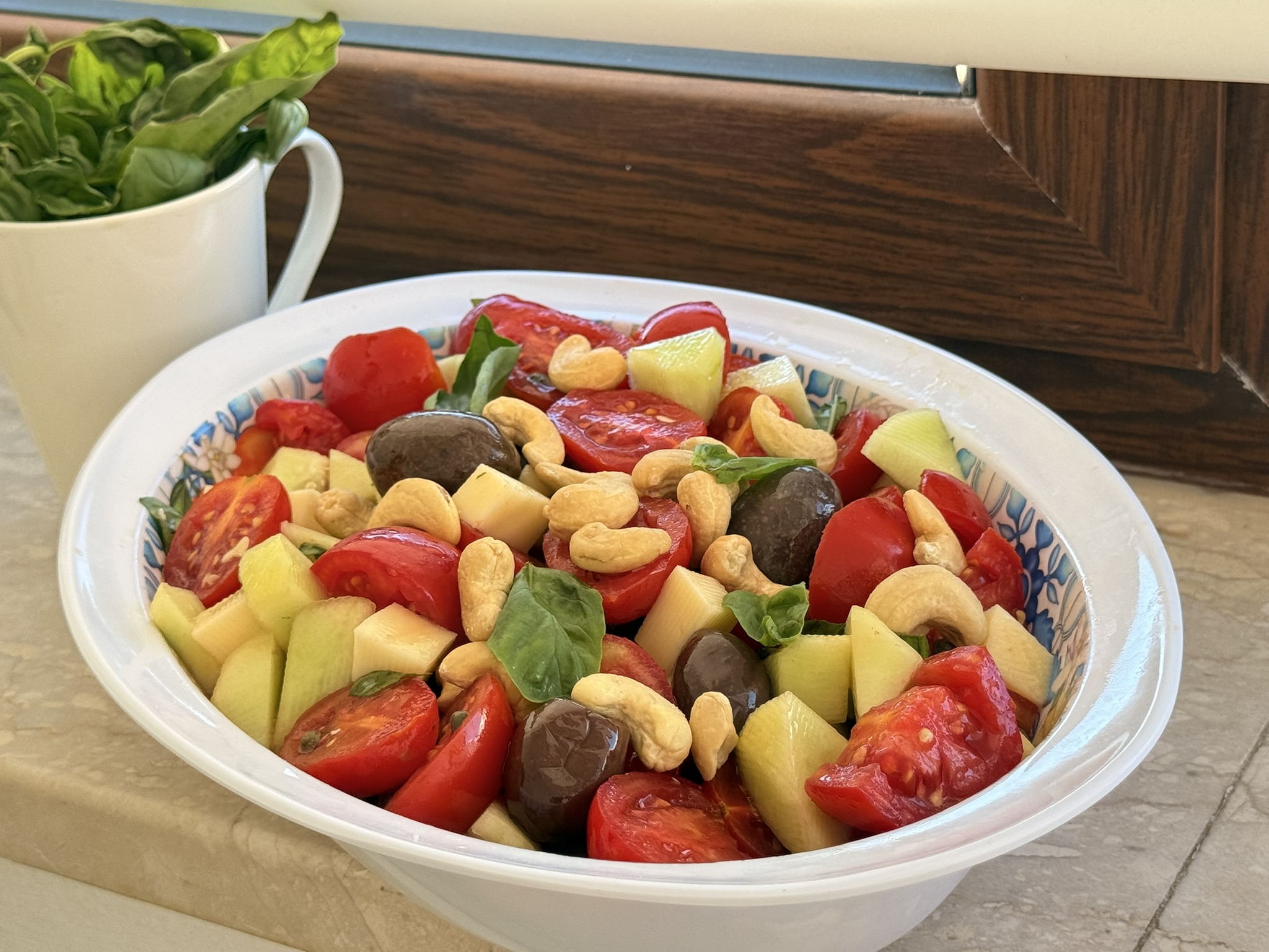 insalata pantesca: ricetta fresca e sfiziosa a modo mio, con pomodorini rossi, cetriolo carosello, olive, capperi, formaggio a dadini, anacardi e basilico fresco. Servita in una ciotola ovale