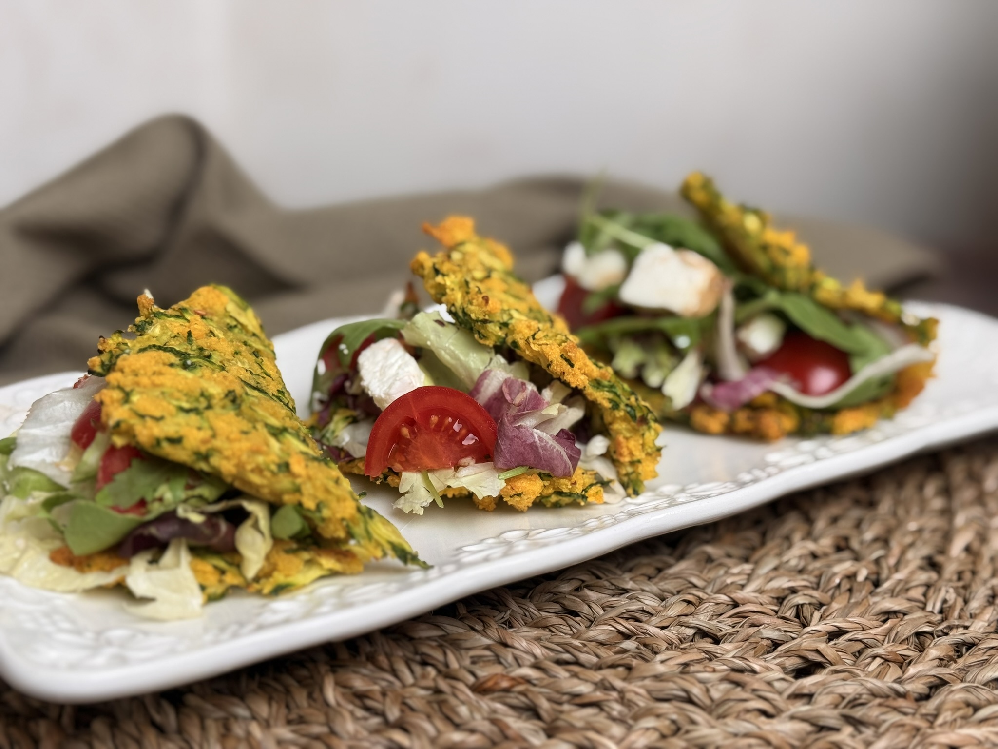 Tacos di zucchine facili e veloci con 3 ingredienti, farciti con insalata, pomodorini e formaggio fresco, disposti su un piatto bianco decorato.